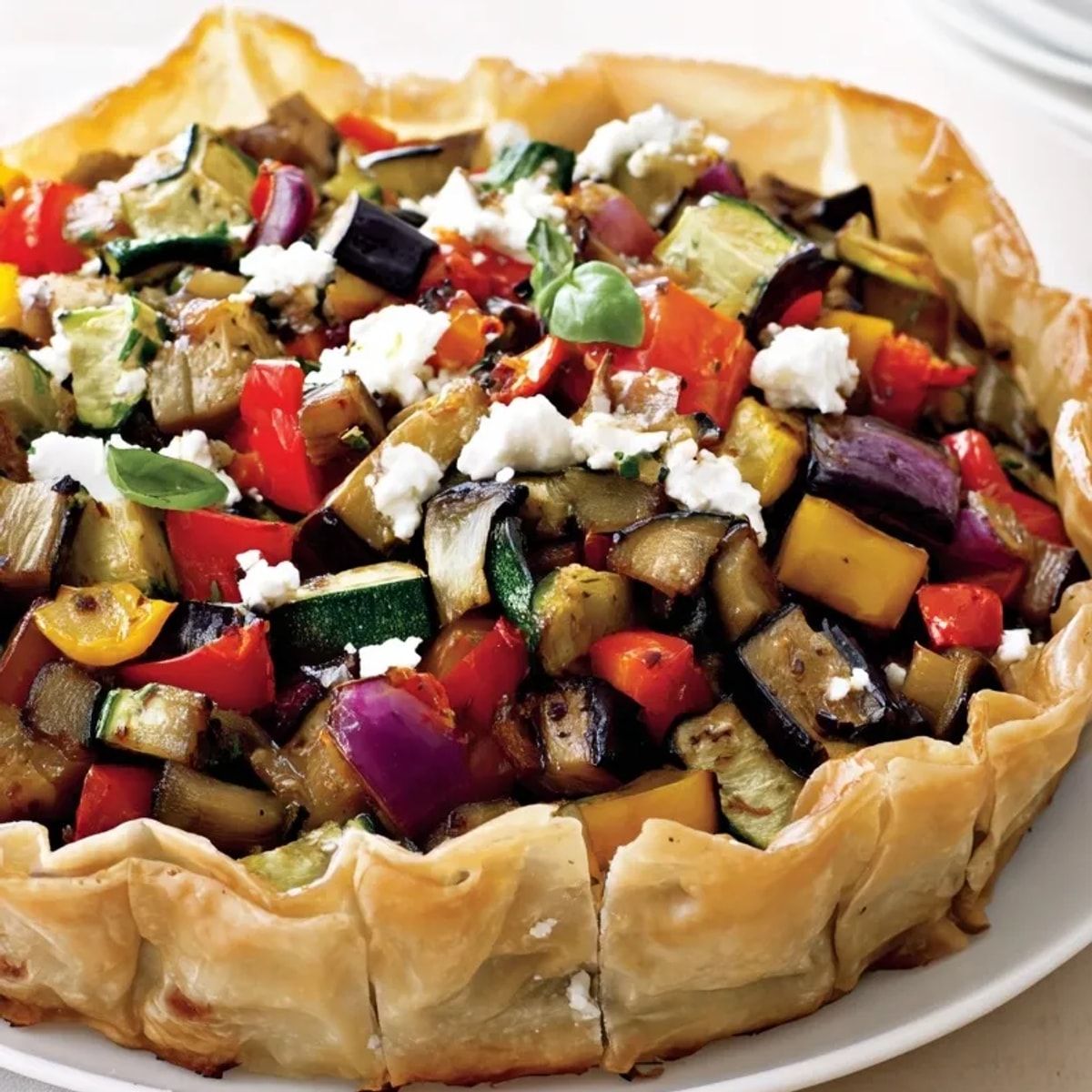 Une tranche généreuse de Tarte Ratatouille Rustique, avec du fromage de chèvre crémeux fondu sur les légumes rôtis.