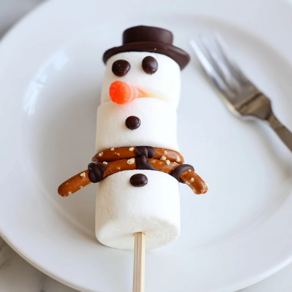 A close-up of Marshmallow Snowman Stick Arrangement, decorated with chocolate faces, pretzels, and orange noses.