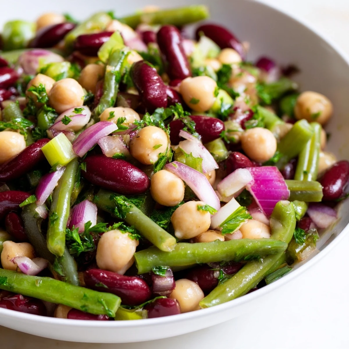 Un bol coloré de Three-Bean Salad avec haricots verts, rouges et pois chiches, relevé de vinaigrette piquante.