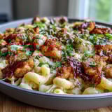 Dans une poêle, du poulet sauté nappé de sauce barbecue au miel est mélangé à des macaronis fondants au cheddar, formant un plat principal américaine réconfortant et savoureux.