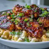 Poulet en morceaux nappé de sauce barbecue au miel, mélangé à des macaroni crémeux dans une poêle prête à servir.