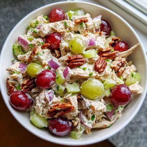 Un plat de salade contenant des raisins, des noix et des garnitures vertes.