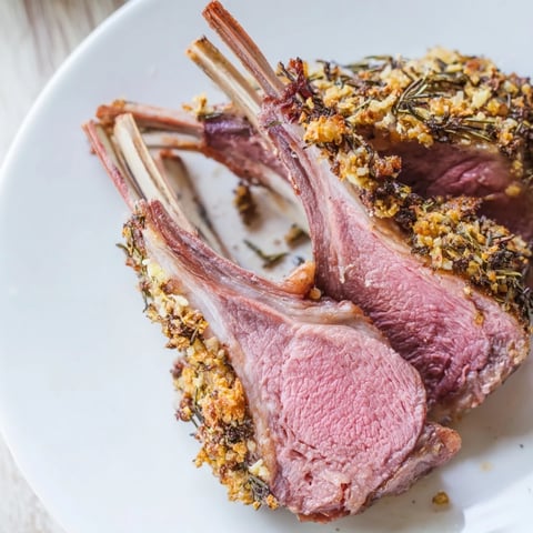 Un rack d'agneau rôti doré sur un lit de pommes de terre aux olives vertes, prêt à être savouré pour un dîner élégant.