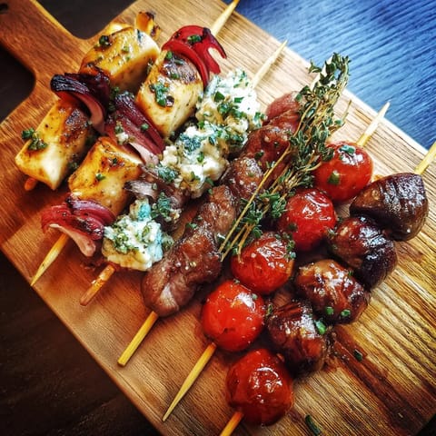 Une table avec des brochettes de viande et des tomates.