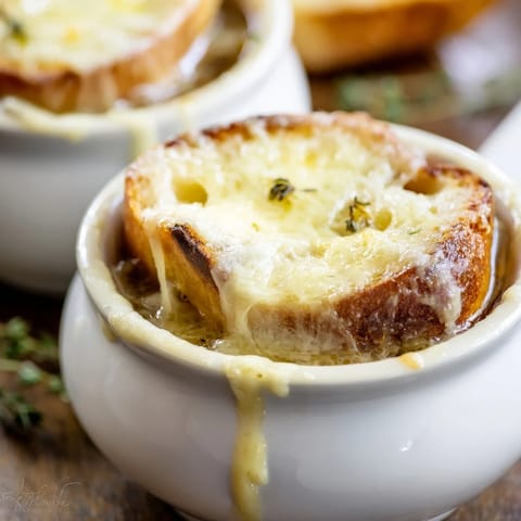 Bol de soupe à l'oignon français garni de baguette dorée et de thym frais.  