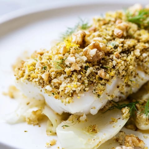 Une assiette élégante de Baked Halibut With Fennel, Lemon and Walnut Pangrattato, servie avec une salade verte.