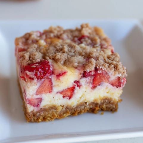 Dessert de pique-nique pour les barres de cheesecake aux fraises, recouvertes de streusel doré et de morceaux de fruits frais.