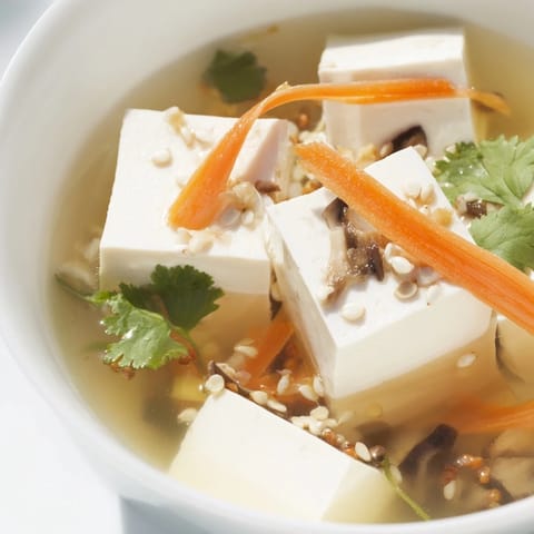 Soupe asiatique légère au tofu et légumes, avec bok choy et champignons, servie avec un quartier de citron vert.