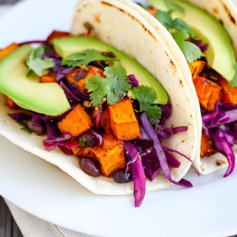 Une assiette généreuse de tacos végétaliens aux haricots noirs et patates douces garnie de chou rouge, avocat et lime.