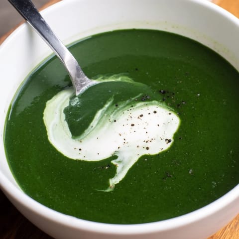 Un bol fumant de velouté d'épinards, agrémenté d'une légère crème en spirale et de poivre noir moulu.