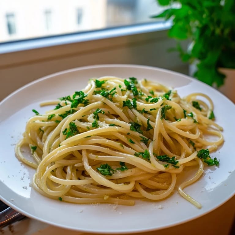 Steaming bowl of pasta with garlic, olive oil, and parsley, garnished with fresh herbs and citrus zest.