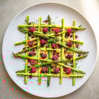 A botanical lattice appetizer featuring vibrant asparagus, fresh berries, and delicate chives artfully arranged.