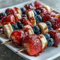 Brochettes de fruits rouge, blanc et bleu pour le 4 juillet, avec des fraises juteuses, des bananes et des myrtilles.